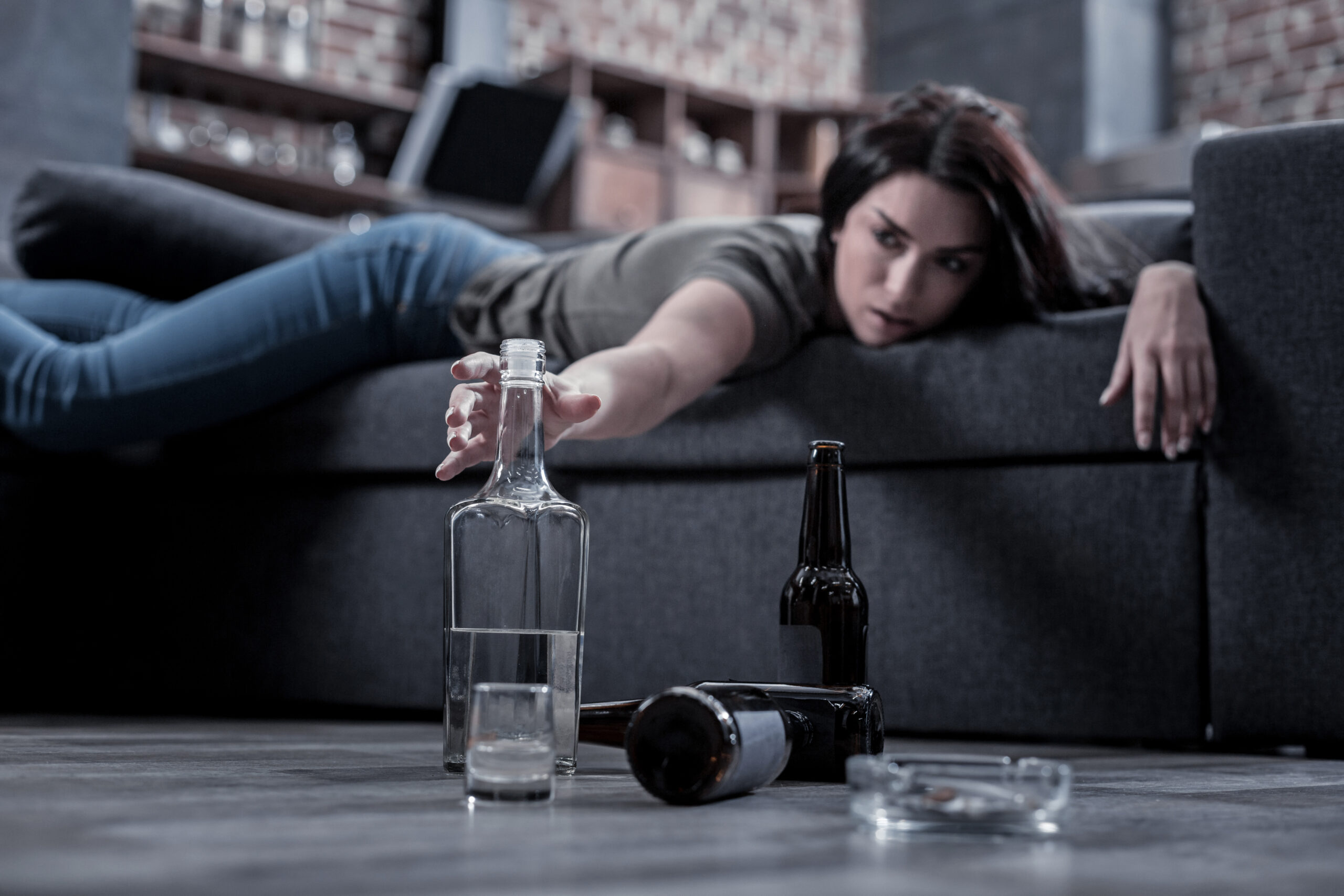 alcool, une femme allongée sur un canapé attrape une bouteille.