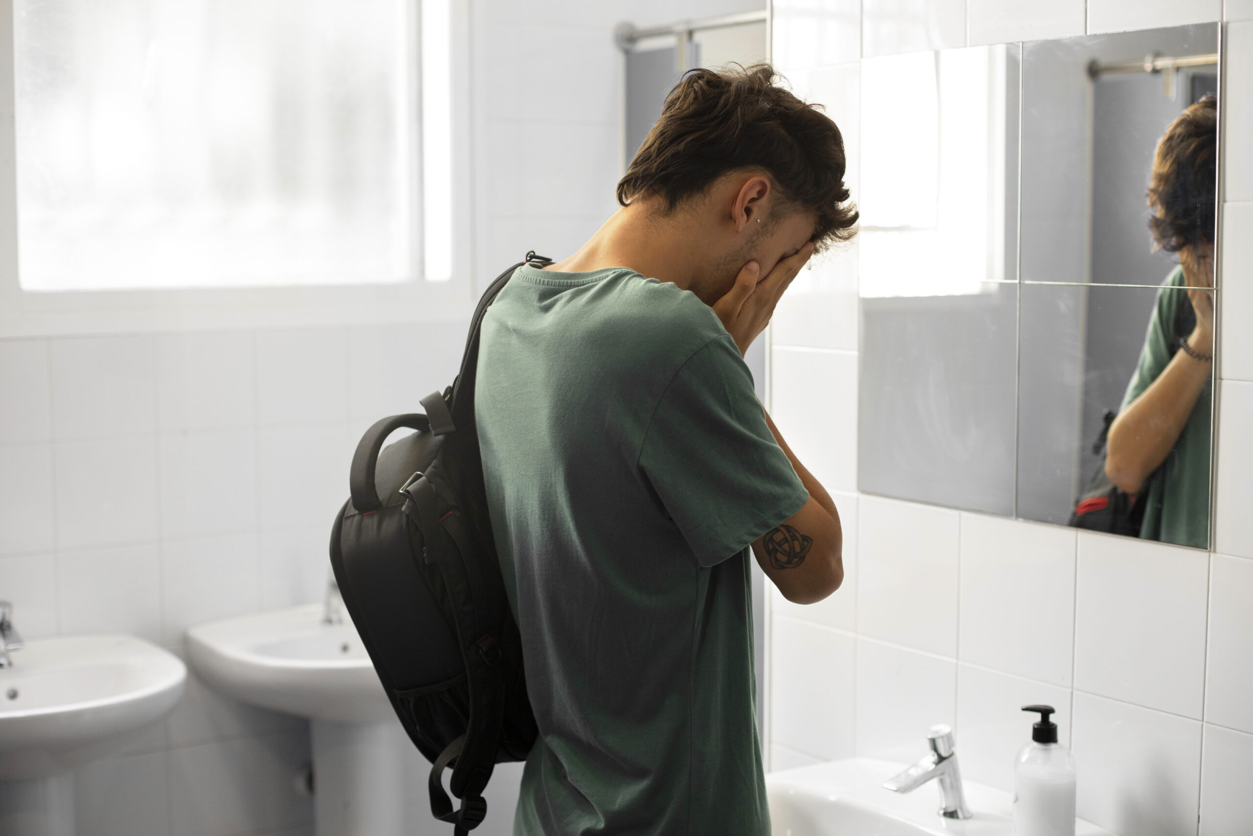 Phobie scolaire, un jeune homme pleure devant le mirroir des toilettes du WC dy lycée